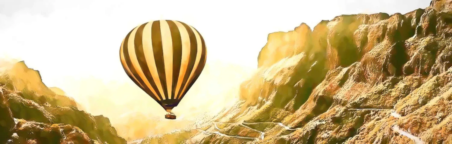 Hot air balloon rising over hillside wth road showing the direction forward