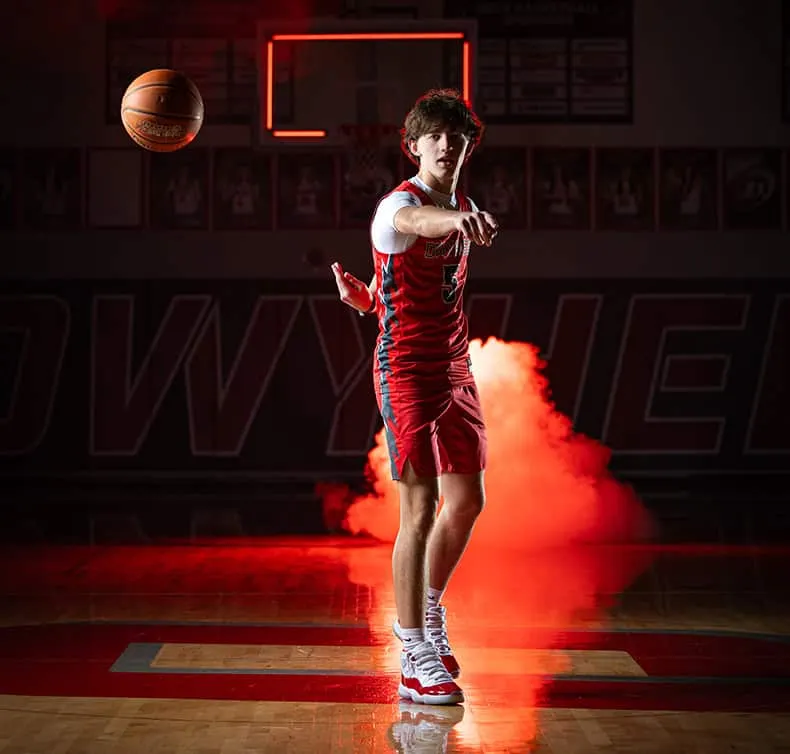 Owyhee Basketball player in red uniform making no-look pass on court with dramatic red lighting and smoke effects, high school sports photography