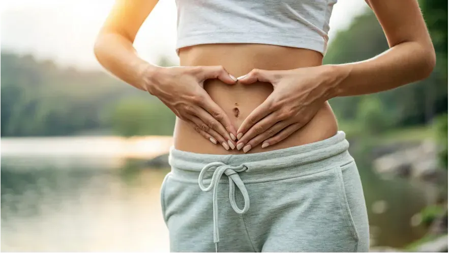 a woman's midsection, with her hands forming a heart shape over their stomach.