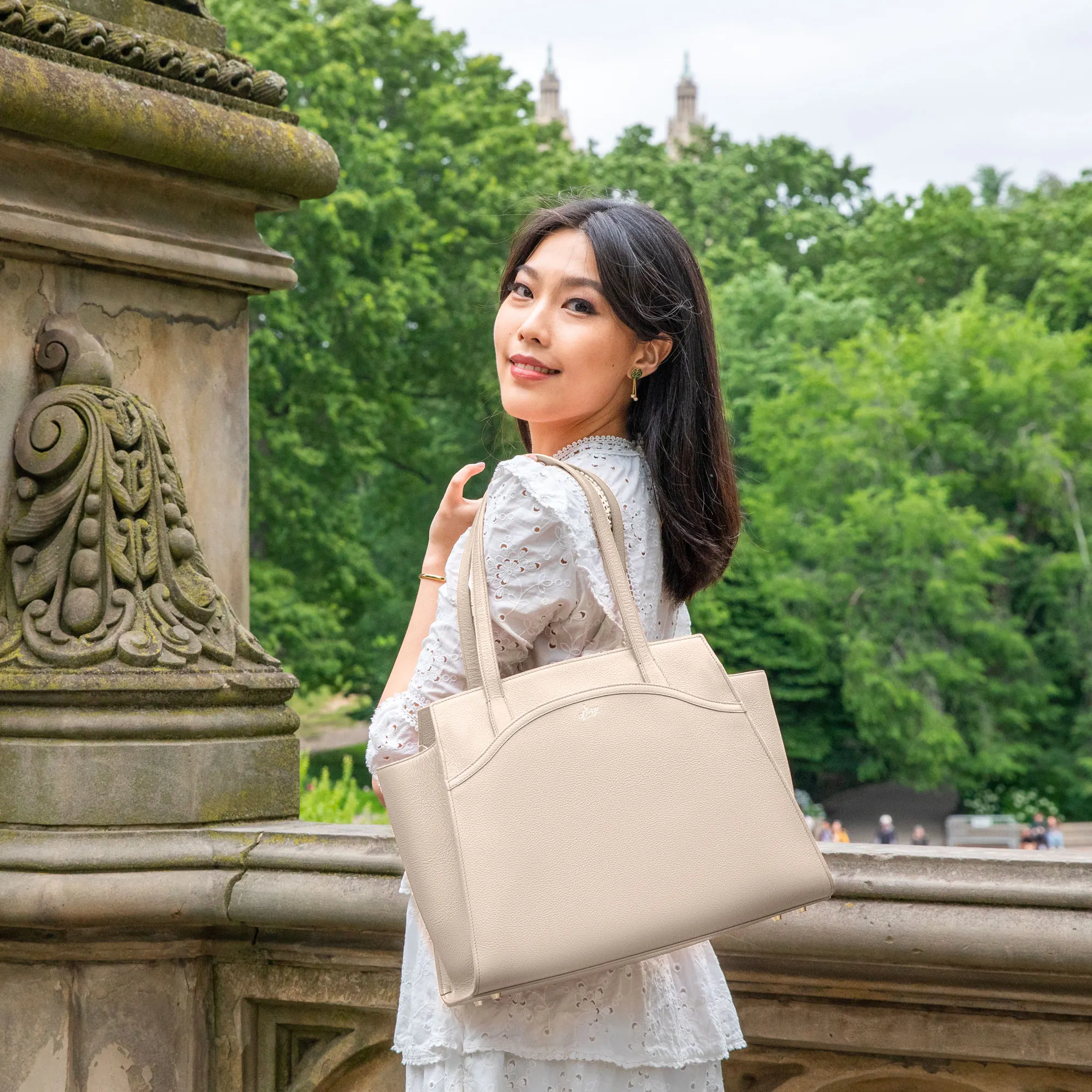 An elegant lady is wearing a parchment beige Tang Dynasty Grace Tote, a bag that is inspired by Tang Dynasty, designed by Shen Yun Collections, made in Spain. 