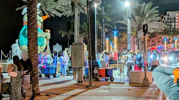 crowd on a brightly lit streetcorner close to a giant snowman, palm trees decorated in lights