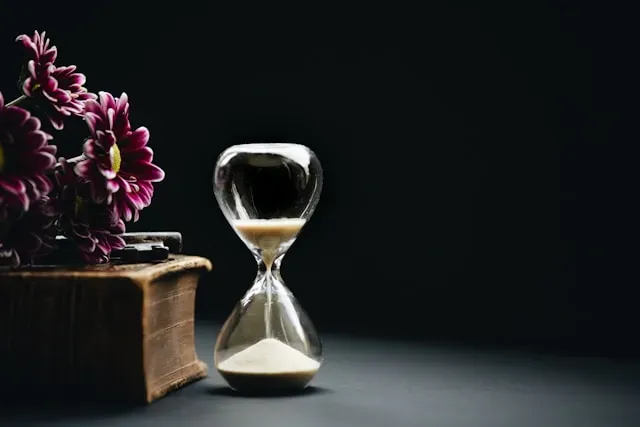 hourglass in the spotlight next to fresh flowers denoting owning your time