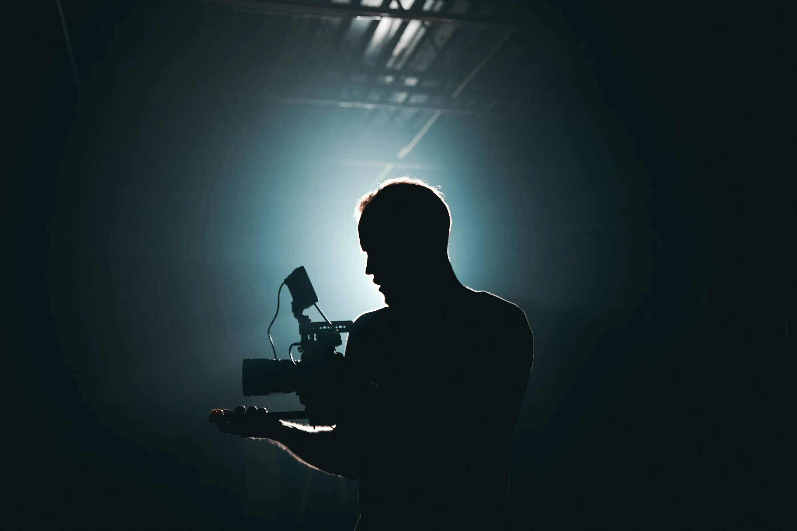 a man holding a camera rig in a low-lit, cyan lighting environment
