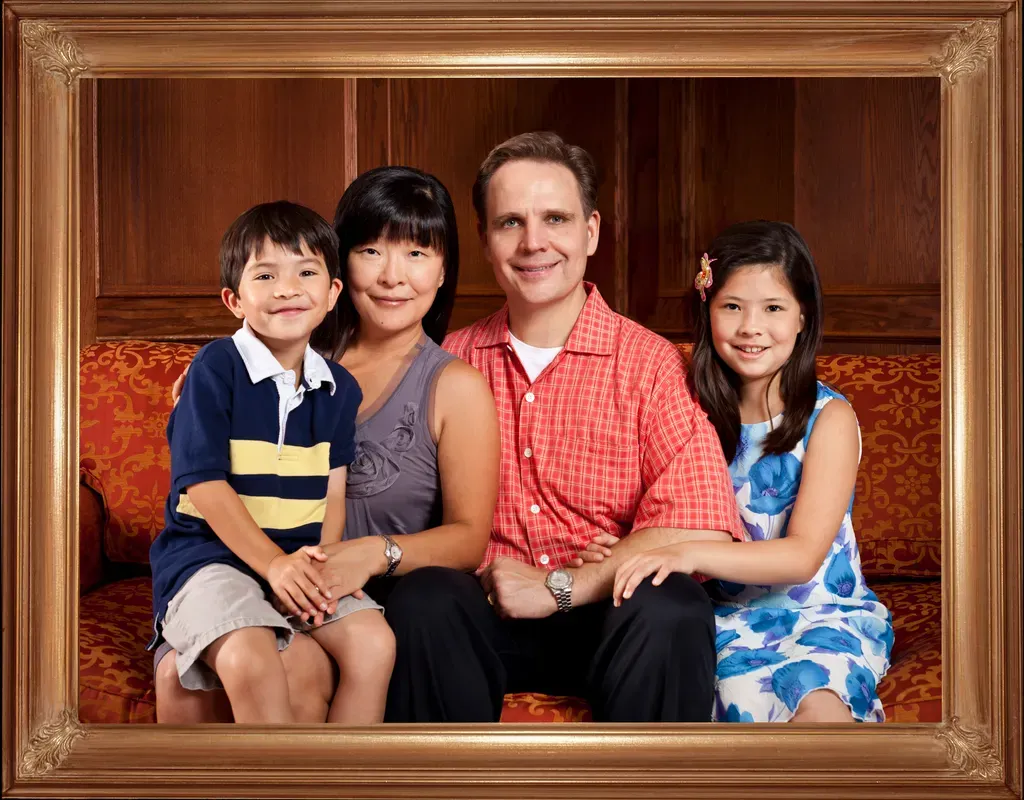 Family of four—dad and mom, together in the middle with children on either side (a boy and a girl) sitting on a couch.