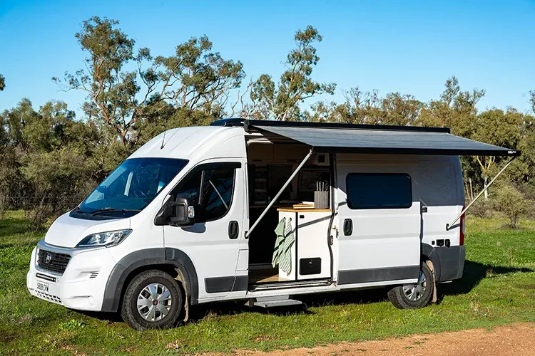 White Fiat Ducato campervan with awning extended in the Australian bush, showing exterior layout of Matthew Storer’s self-built van