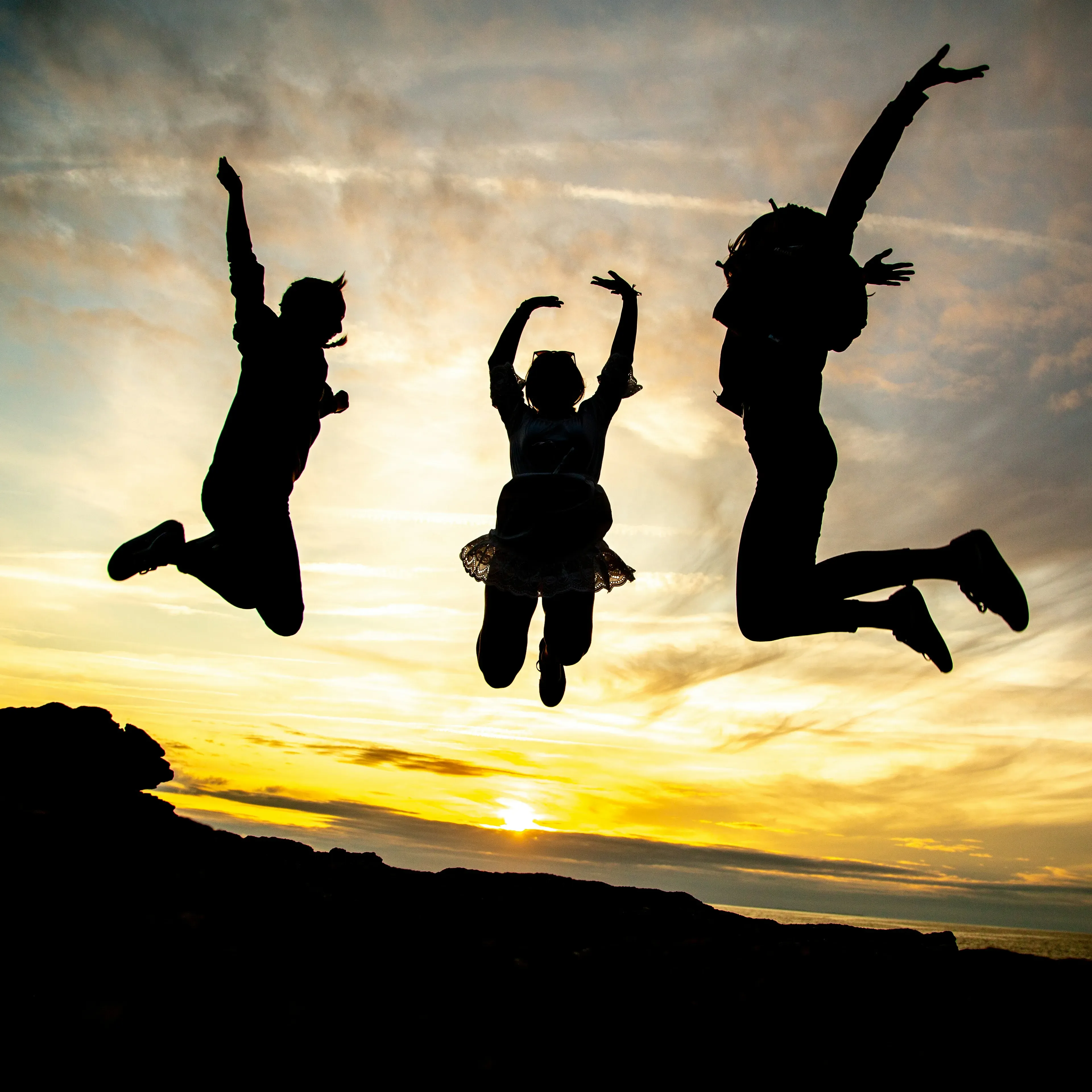 3 people silhouettes jumping freely with golden sky background