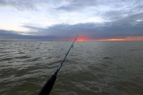 Fishing rod casting into calm ocean at sunset from shoreline