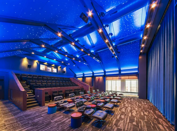 movie theater with leather recliners in front and traditional movie theater seating behind.  Blue lit ceiling