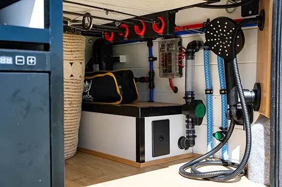 Campervan plumbing system with water pump, filtration, hoses, and outdoor shower setup for off-grid travel