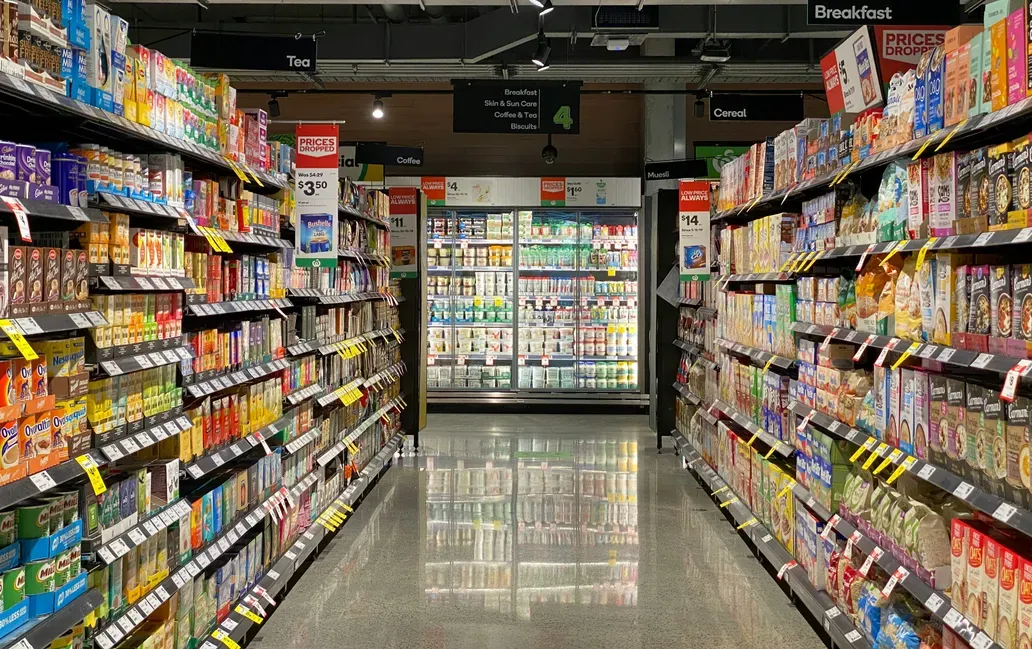 Grocery store aisle with shelves of teas and coffees on the left and refrigerated dairy products on the right, under signs for related products and categories.