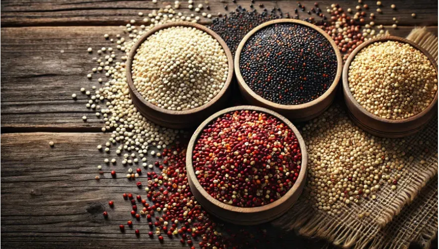 a variety of quinoa grains (white, red, black) displayed in separate bowls on a rustic wooden table, with a few grains scattered around to show texture.