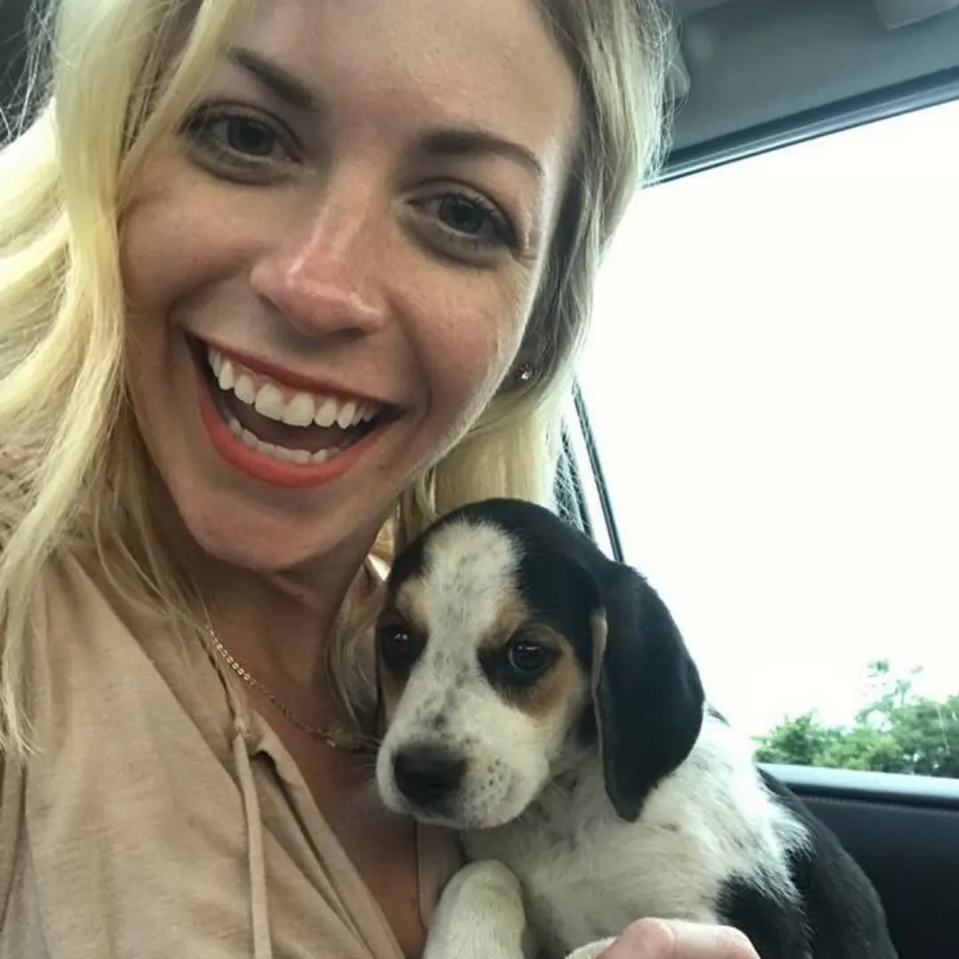 Dog owner smiling with her beagle puppy after receiving compassionate positive reinforcement training from Newman's Dog Training, focused on relationship-building over harsh correction.