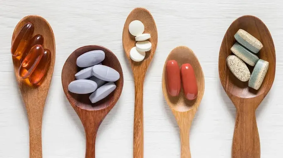 Four wooden spoons arranged diagonally, each containing different types of supplements.