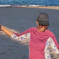 torso of woman wearing cap, sunshades, longsleeve shirt , on the beach