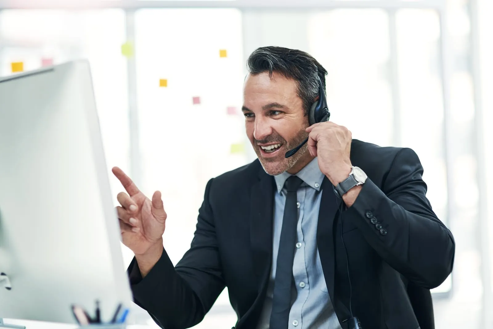 hombre-profesional-con-auriculares-haciendo-gestos-mientras-mantiene-una-conversación-en-el-escritorio-de-su-computadora-como-vendedor