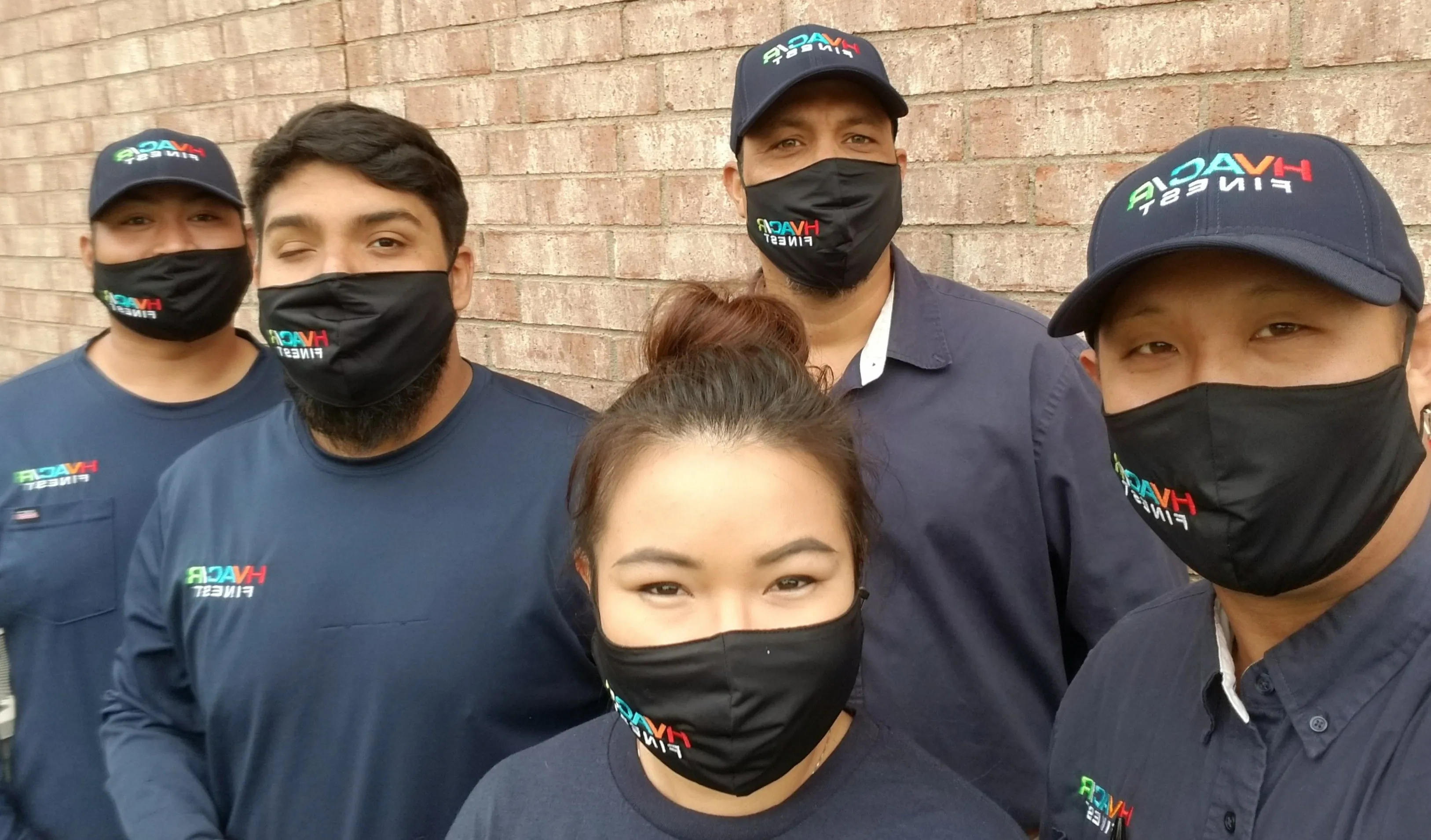 Five individuals wearing face masks stand together beside a brick wall, emphasizing safety and community during a health crisis.