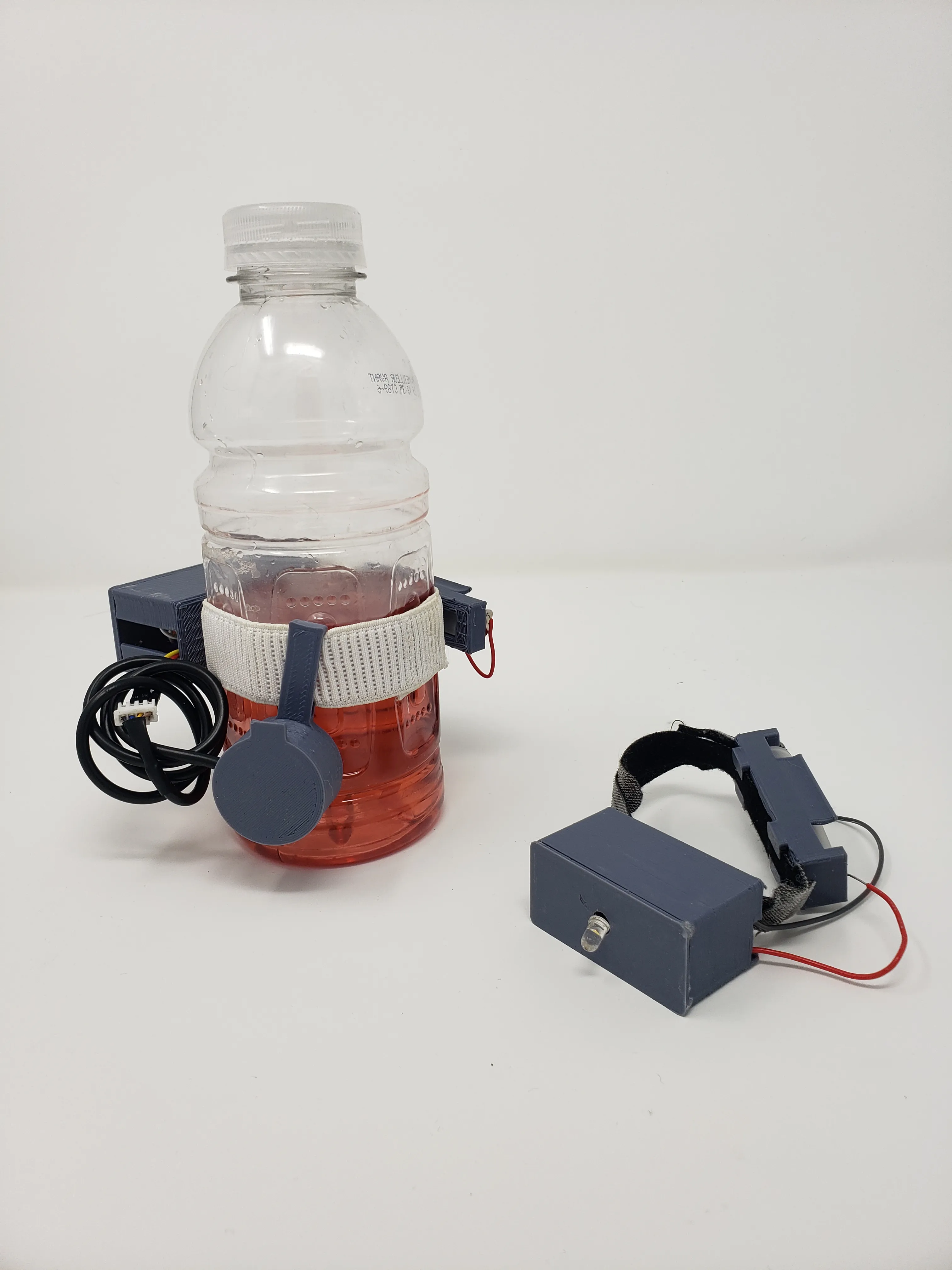 bottle filled with liquid higher than the non contact fluid sensor that is held onto the bottle with an elastic. Beside the bottle is a wrist band with an led off. 