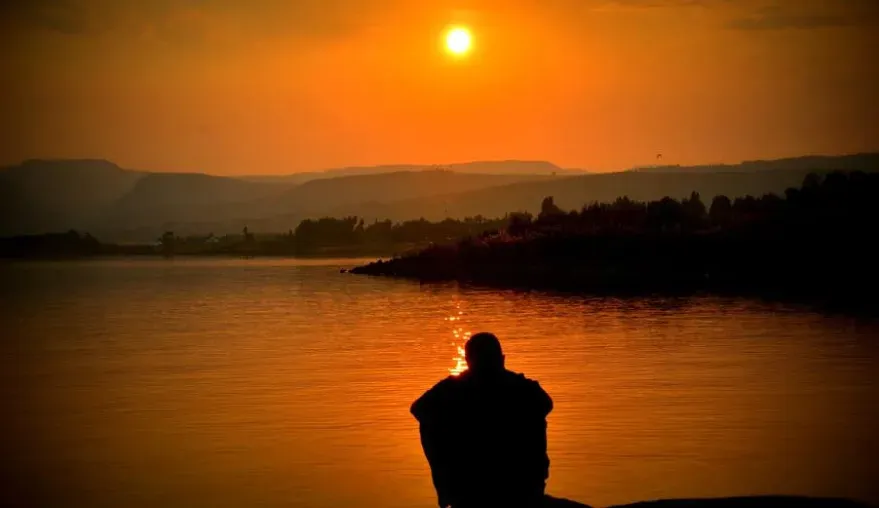 A man sitting peacefully on a serene lake as the sun goes down.