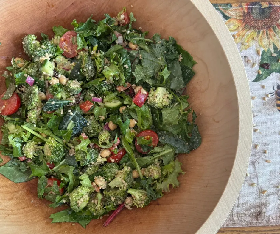 Leafy green salad topped with broccoli quinoa salad, cucumber, tomatoes, sunflower seeds, and a drizzle of balsamic vinegar.