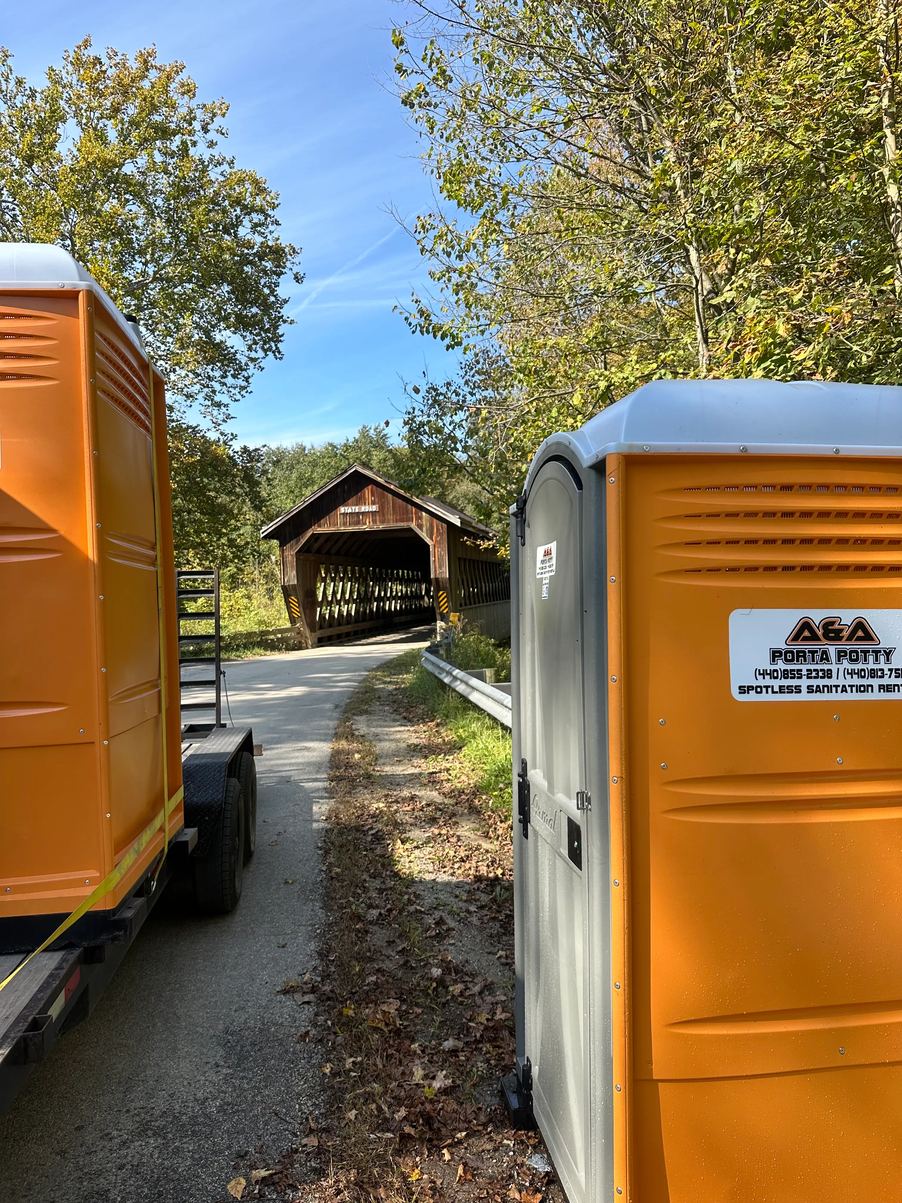 Orange portable restrooms on a trailer in front of a covered bridge for delivery