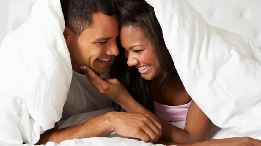  a playful and adventurous couple in a private setting, under the covers in bed.