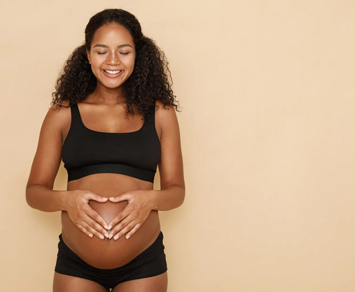 woman in bathing suit showing a heart over her pregnant belly