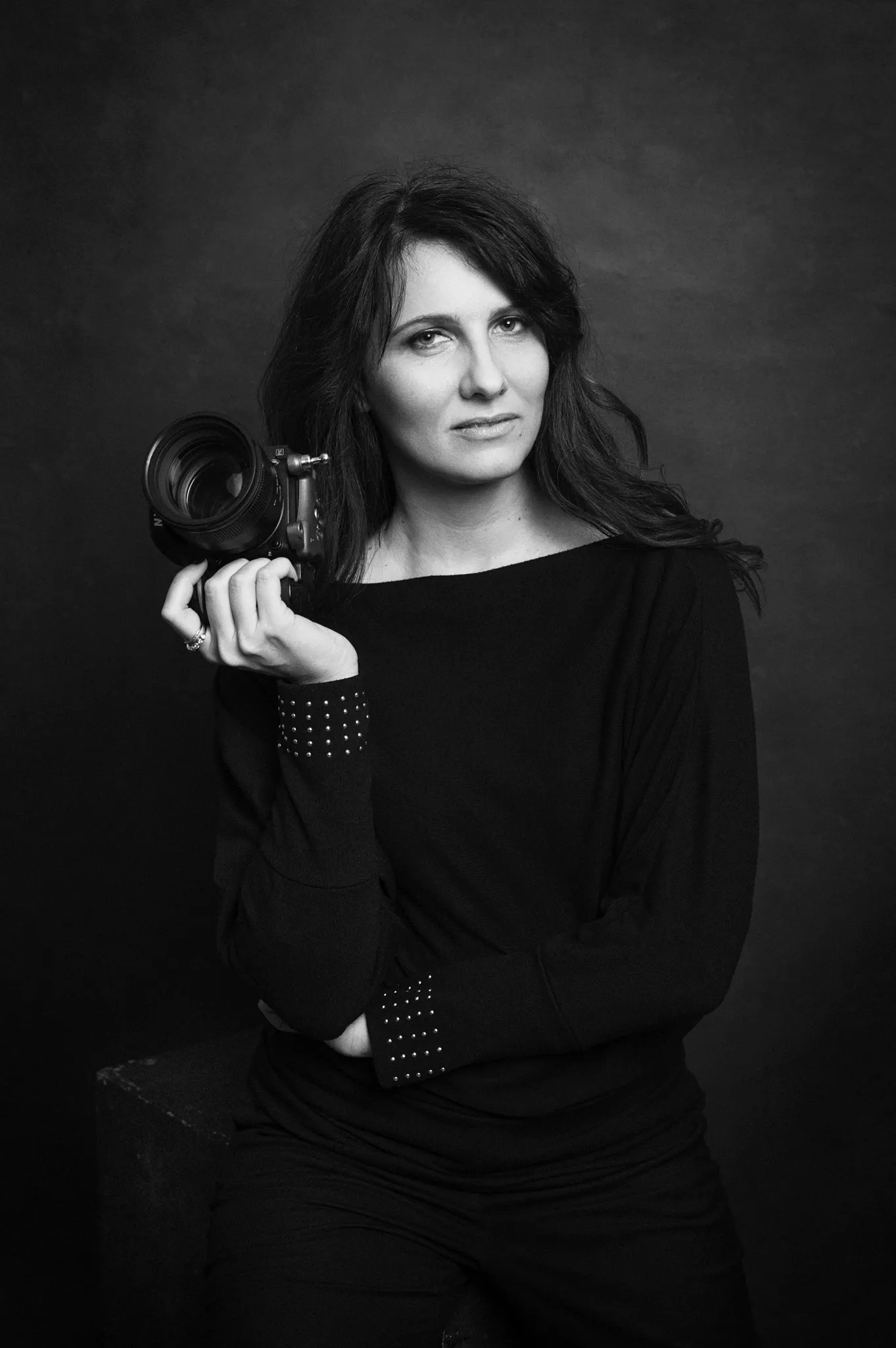 fotografa di ritratto Milano Federica Nardese - fotografia di professionista fotografa, vestita di nero, su sfondo pittorico scuro, macchina fotografica in mano.