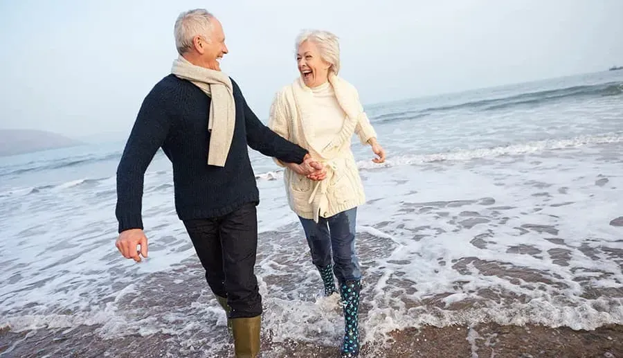 A late middle aged man and woman smiling and having fun on a beach.