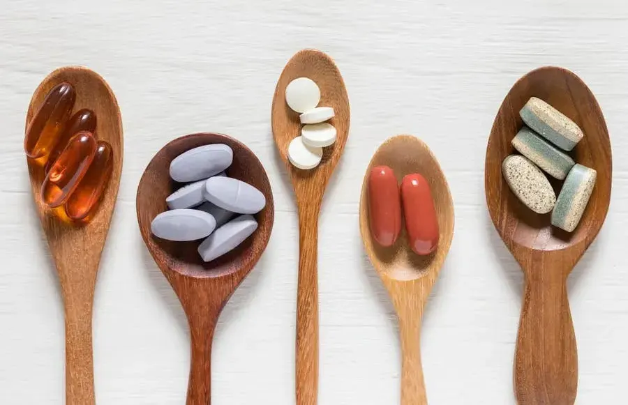 Four wooden spoons arranged diagonally, each containing different types of supplements.
