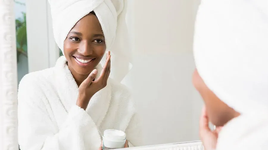 A woman in front of the mirror rubbing cream on her face.