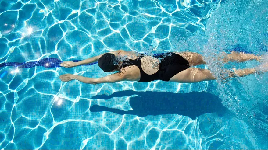 Woman in bathing suit and cap swimming underwater. 