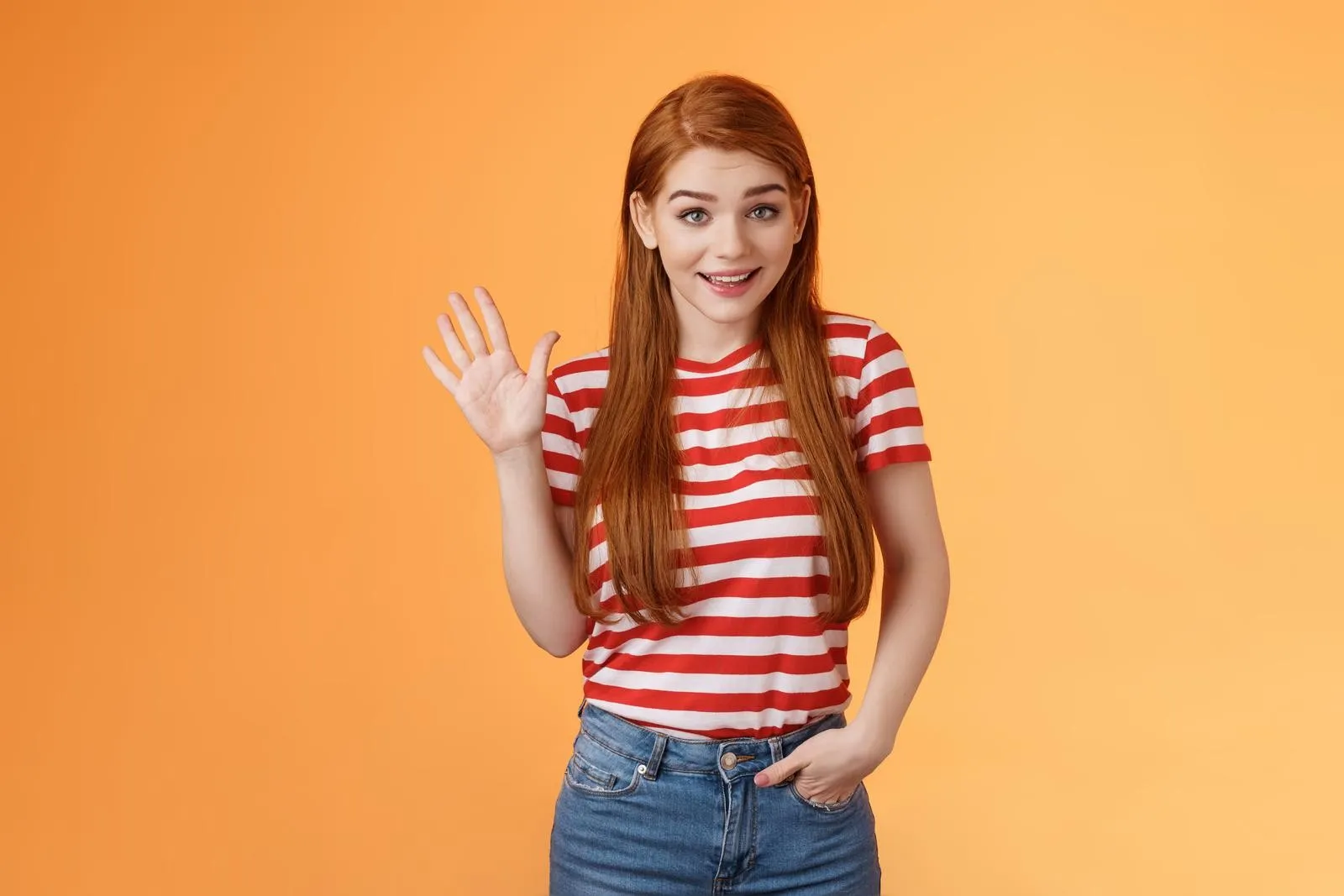 una-mujer-joven-con-una-camisa-a-rayas-sonriendo-y-diciendo-adios-sobre-un-fondo-naranja