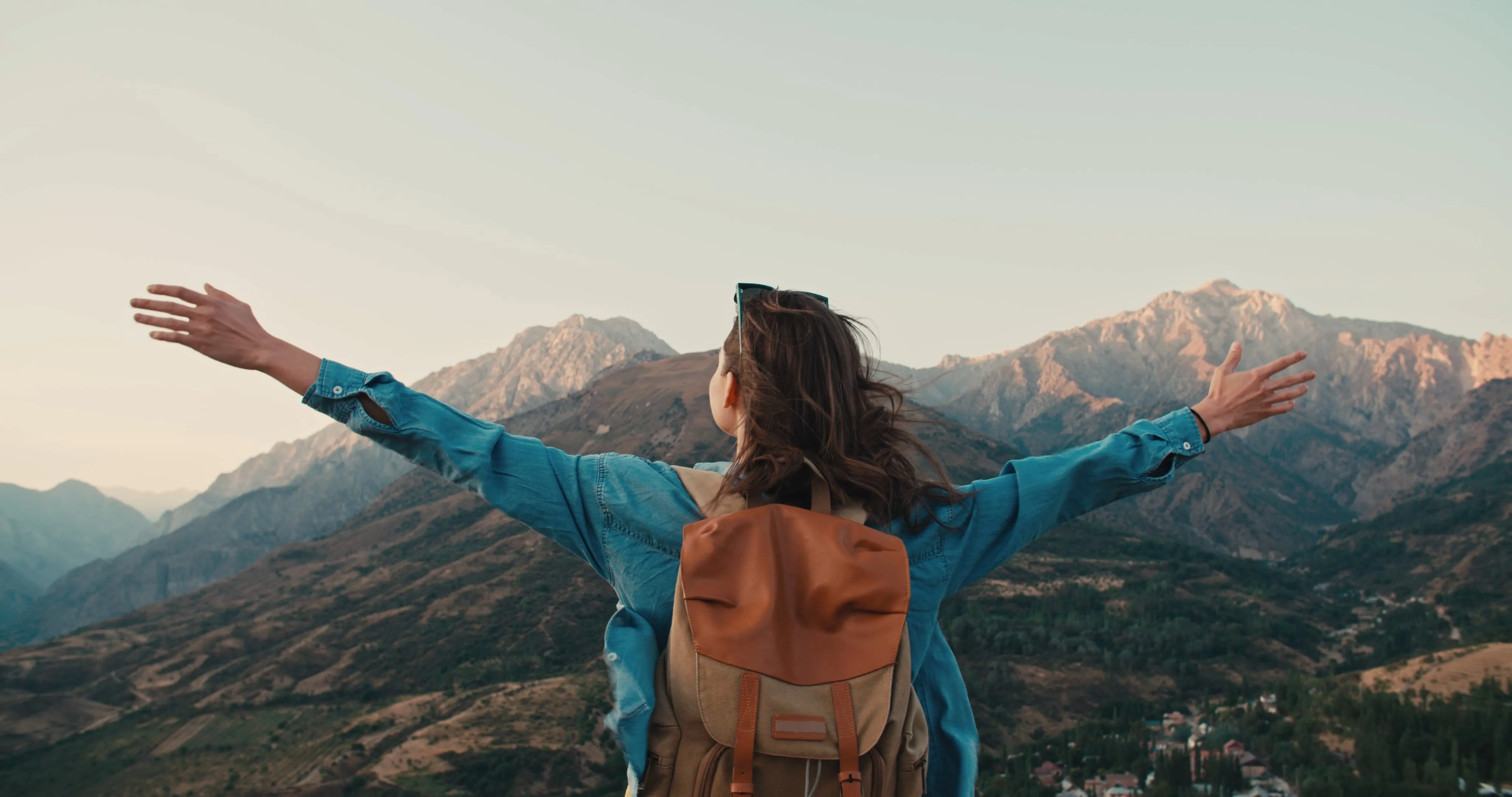 Woman wearing a backpack standing on a mounting with her arms spread out enjoying the scenery