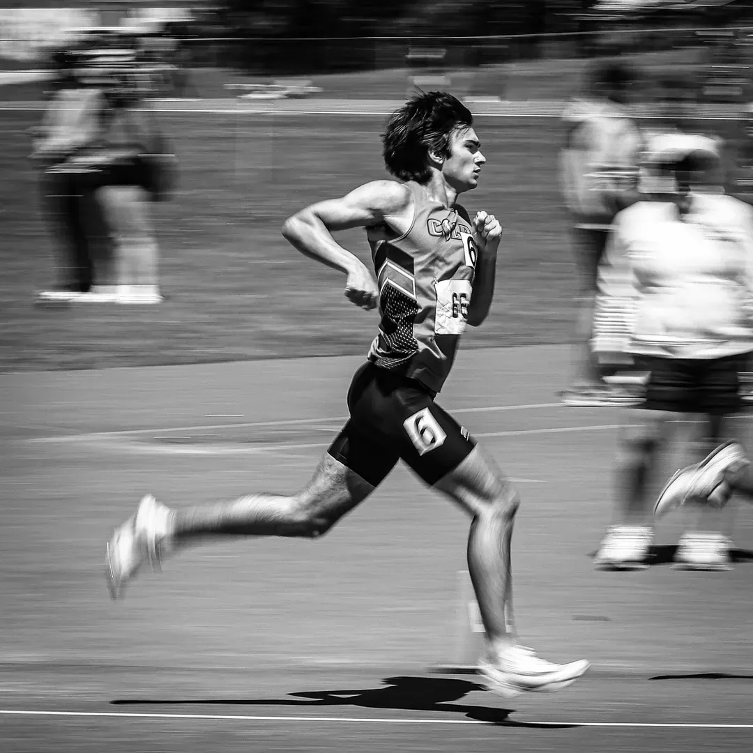 A high contrast black and white photography of a high school athlete running a track event