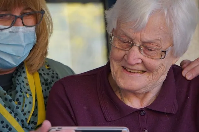 Caregiver showing old woman something on her phone