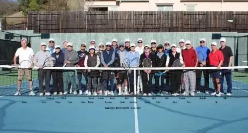 A group of seniors posing behind a tennis net