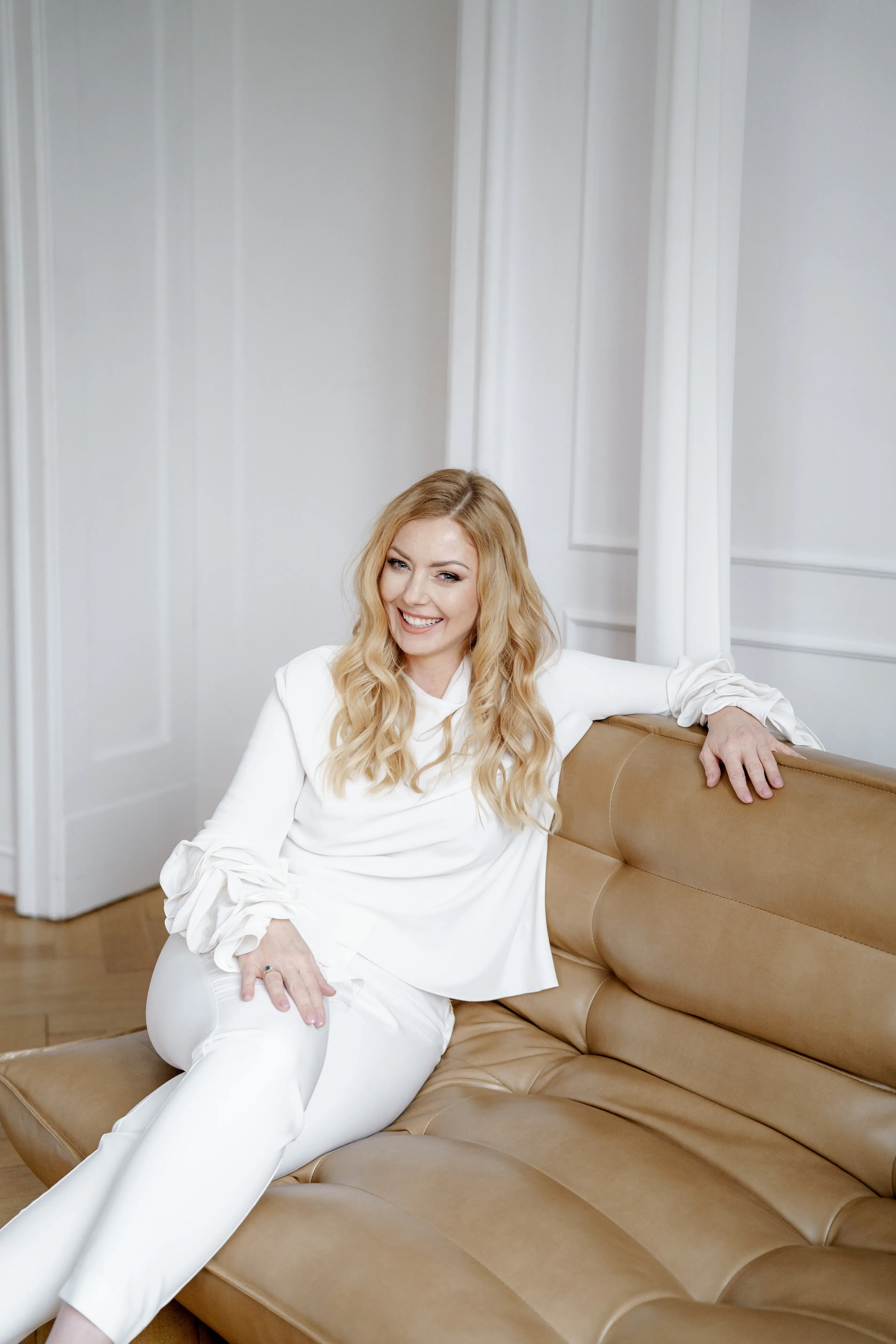 A beautiful blonde woman with a wavy hair sitting on a brown sofa