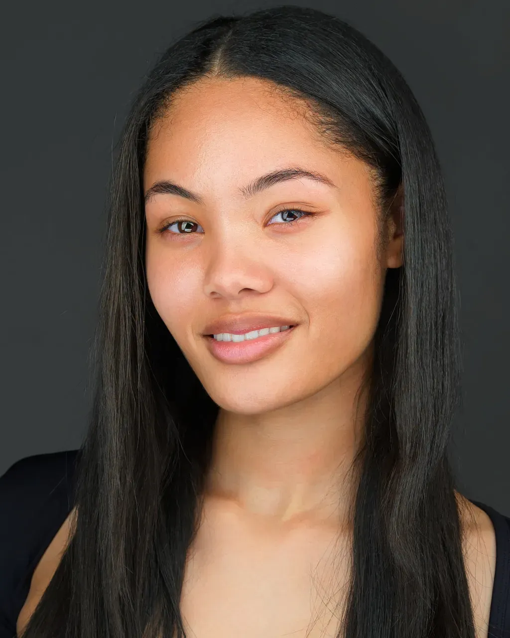 Dark skinned woman posed for a headshot wearing a taupe turtleneck posed in front of a brown backdrop