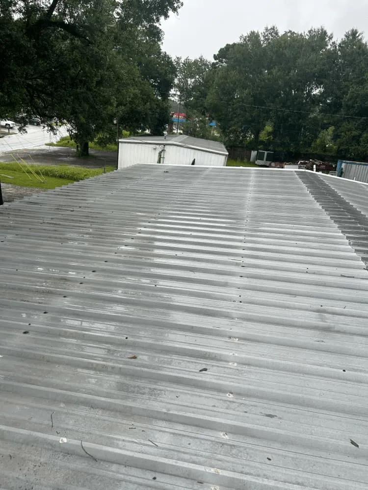<alt=“Commercial roof cleaning results on large building in Theodore, Alabama with surrounding landscape.”>