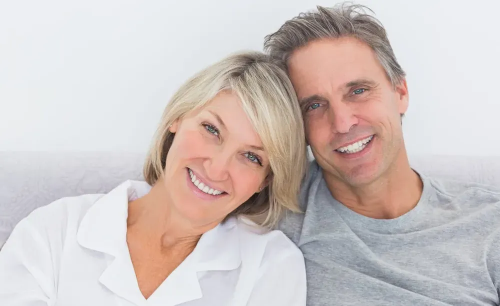 Middle aged couple seated and snuggling together with big smiles on their faces.