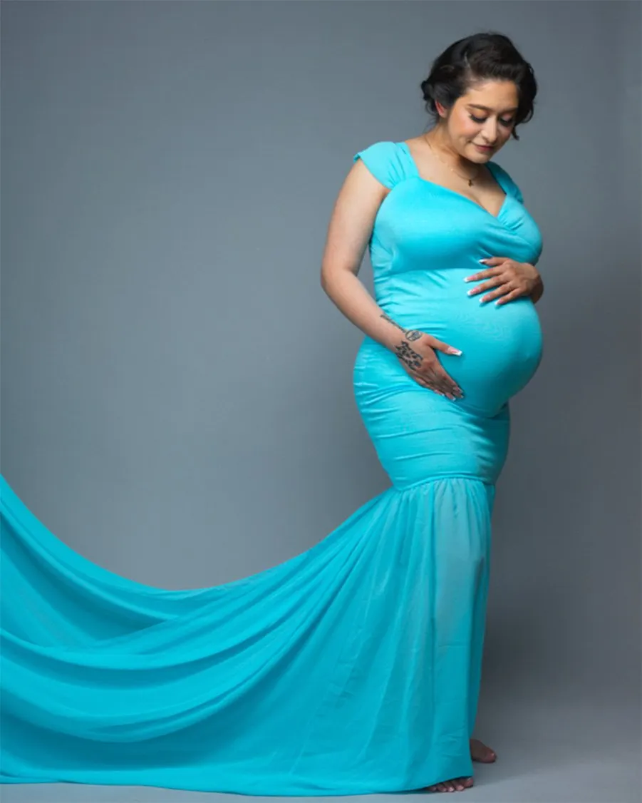 Maternity portrait of woman wearing a long blue gown posed in front of a grey backdrop