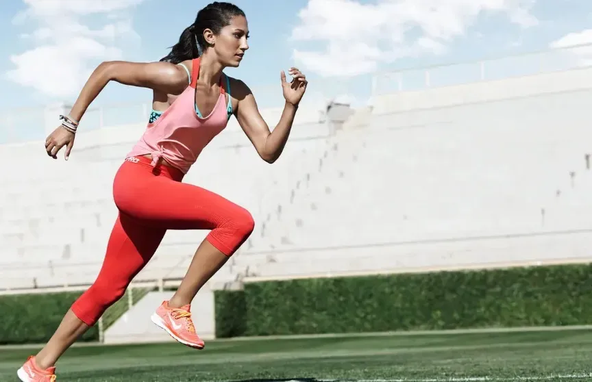 Woman in running gear sprinting on a grass field.