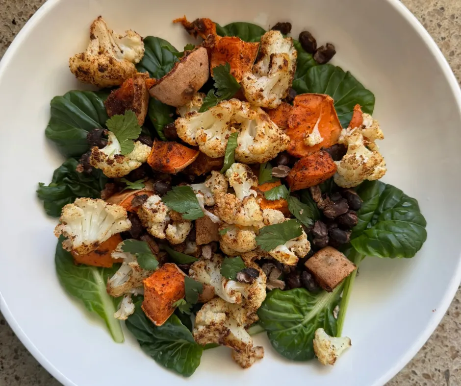 Sheet pan meal with roasted cauliflower, black beans, and vegetables served over greens