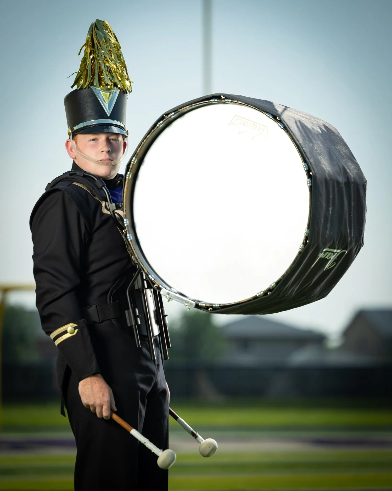 [marching band, percussion, uniform] Marching band drummer in black uniform and tall plumed hat, holding bass drum mallets