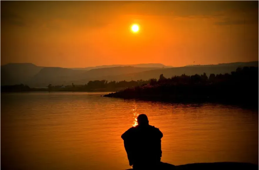 Man sitting on a lake watching the sun set