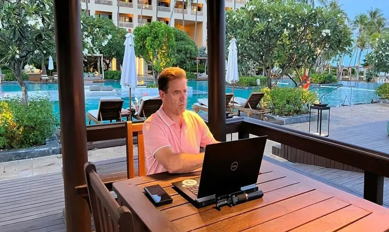 Eric Wheeler sitting at a table with a laptop by a resort pool in exotic vacation location.