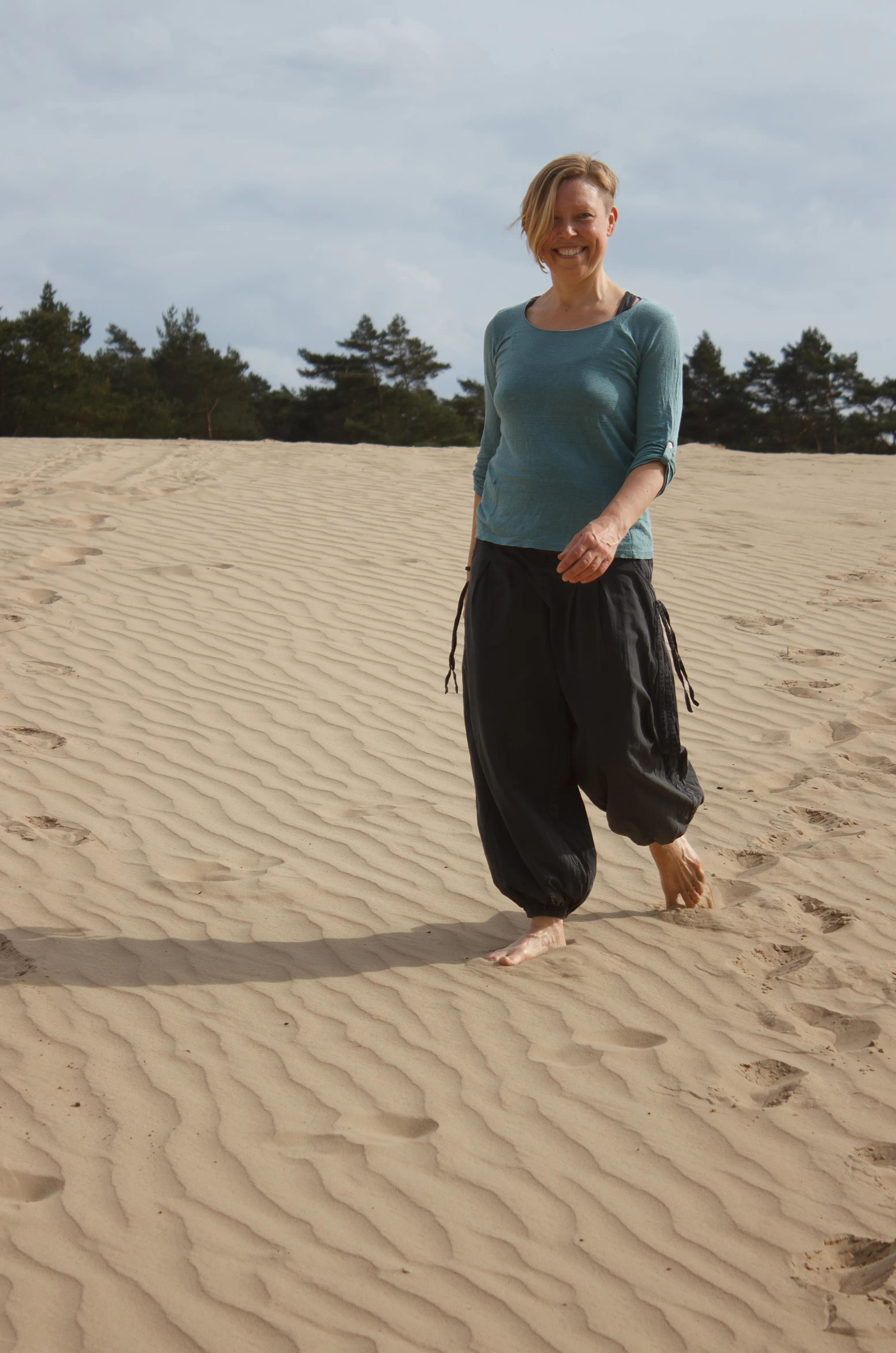 Ingrid wandelt in het zand en glimlacht in de camera