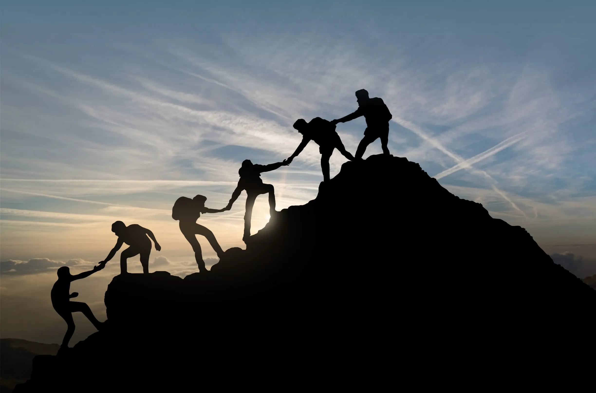 team helping eachother hiking up a mountain