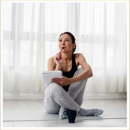 Woman in deep thought sitting on a yoga mat about to write in a journal