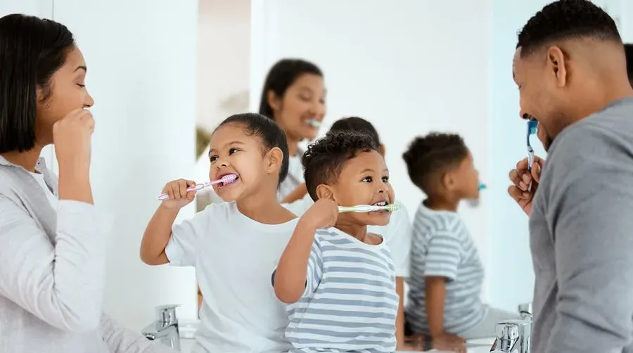 a family of four in the bathroom all brushing their teeth together.